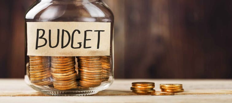 Glass jar with money and a sticker with the words BUDGET, on a wooden table.