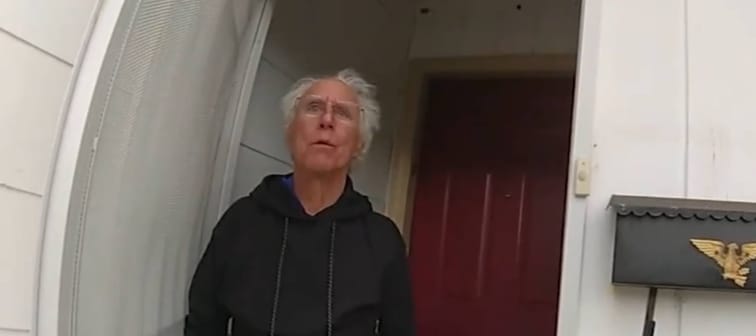 Man with white hair answers front door, looking surprised and concerned.