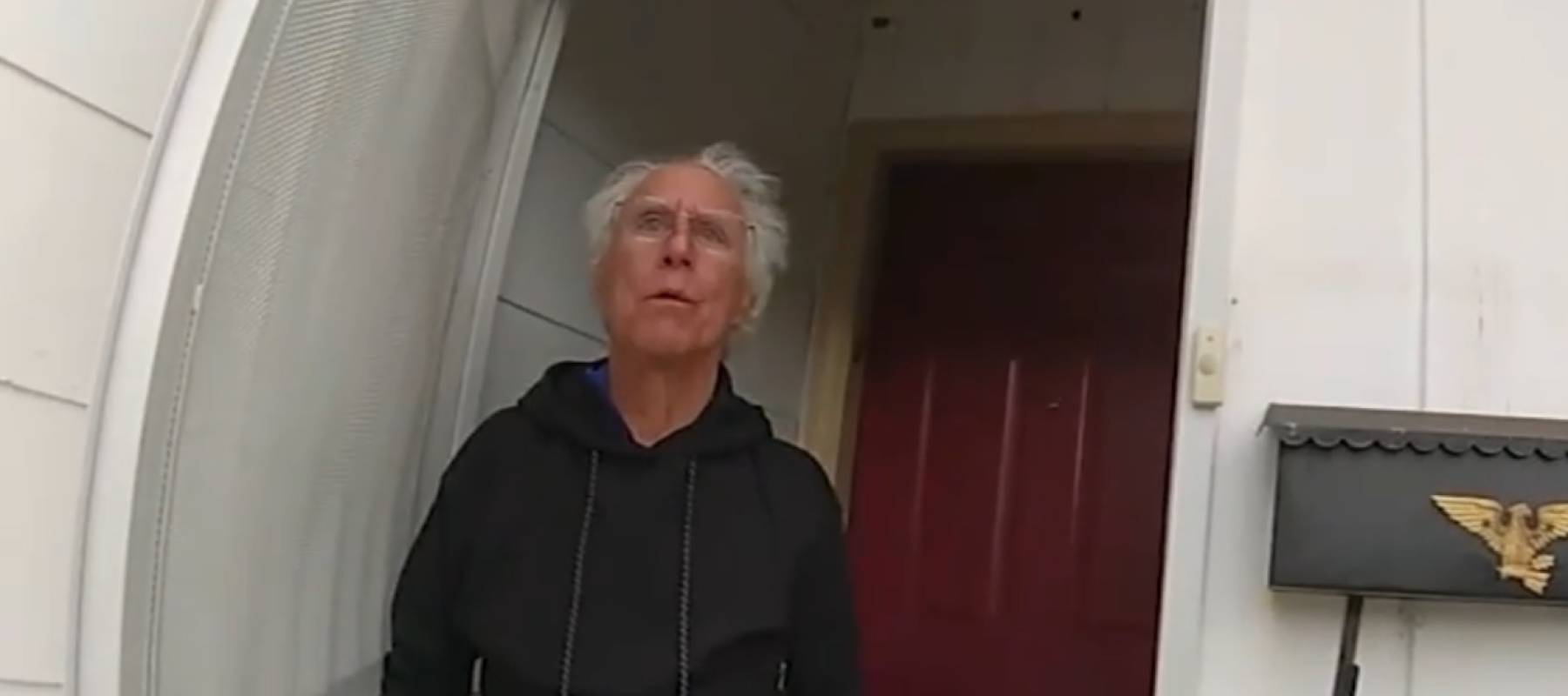 Man with white hair answers front door, looking surprised and concerned.