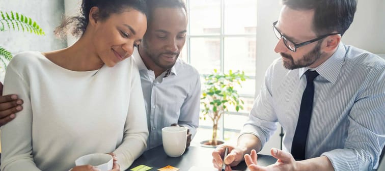 happy couple hold coffee cups and look at paper as man explains something to them