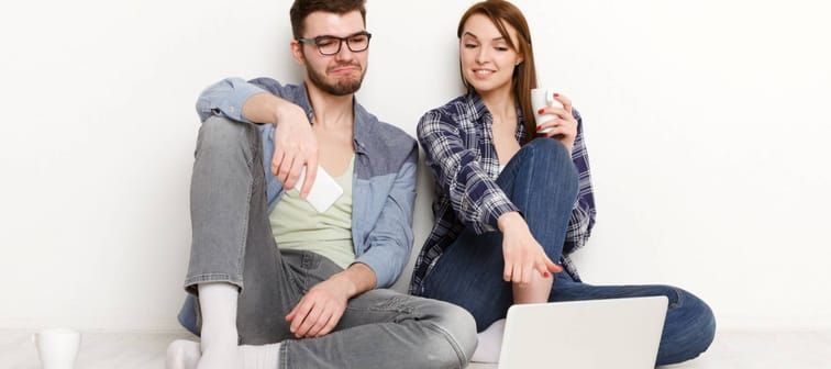 Online order. Couple shopping on laptop at food delivery while sitting on floor at new apartment, white background