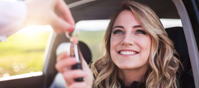 A woman getting the keys to a car while sitting in the driver's seat