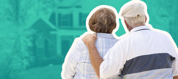 A headshot of a happy elderly couple standing in front of a house