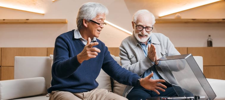 happy senior friends listening vinyl record while sitting on couch