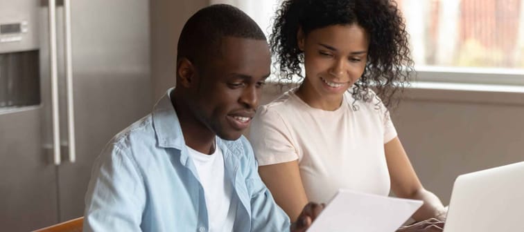 Happy man and woman sitting at kitchen table, looking at paper